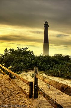 a light house sitting on top of a beach next to a wooden fence and trees