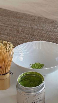 matcha powder in a white bowl next to a bamboo whisk on a table