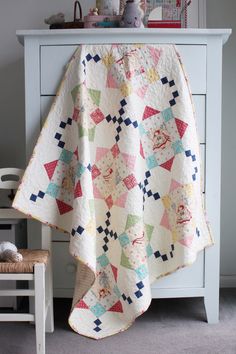 a quilted blanket on top of a dresser next to a white chair and table