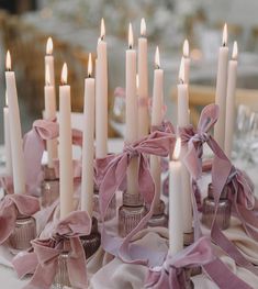 a table topped with lots of white candles covered in pink ribbon and bowknots