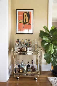 a bar cart with liquor bottles on it and a potted plant in the corner