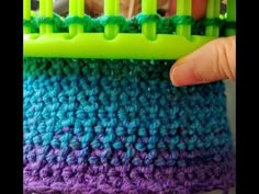 someone is holding up a green and purple crochet piece with yarn on it