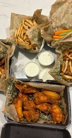 chicken wings and french fries with ranch dips in paper wrappers on a tray