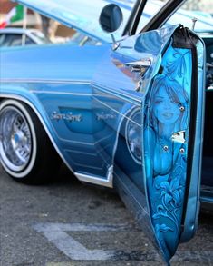 an old blue car parked in a parking lot with its door open to show the side view mirror