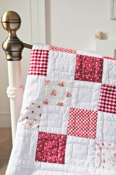 a red and white checkered quilt on a bed next to a night stand with a lamp