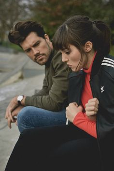 a man and woman sitting next to each other on the ground with their hands together