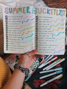 a person holding an open book with writing on it and lots of colored pencils