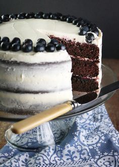 a cake with white frosting and blue berries on top is sitting on a glass plate