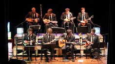 a group of men in suits and ties sitting on stage with guitars, keyboards and microphones