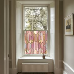 a window with pink and yellow stained glass covering it's windowsill in a white room