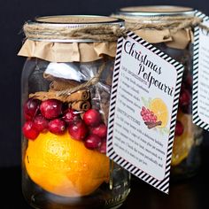 two mason jars filled with oranges, cranberries and christmas recipe tags sitting on top of a table