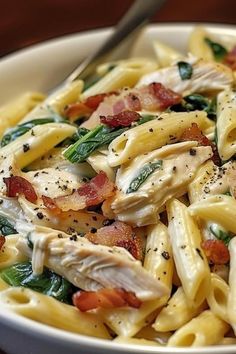 a pasta dish with chicken, spinach and bacon in a white bowl on a wooden table