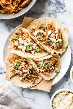 three shredded chicken tacos on a white plate next to bowls of rice and salsa