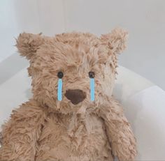 a brown teddy bear with blue tape on it's nose sitting in a bathtub