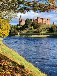 an old castle sits on top of a hill next to a river in the fall