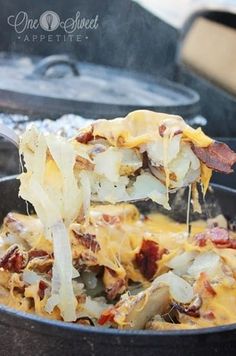 a skillet full of food being cooked on an open fire with a spatula