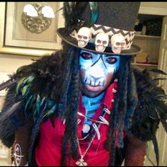 a man with painted face and hair wearing a top hat, feathers and skull decorations