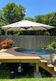 an outdoor hot tub in the middle of a yard with flowers and umbrella over it