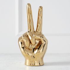 a gold hand statue on a white surface with the peace sign in front of it