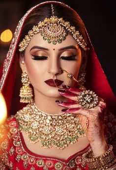 a woman with makeup and jewelry on her face, holding a lit candle in front of her