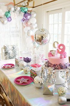 a table topped with a cake covered in pink and purple frosting next to balloons