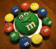 a cake with the letter m on it surrounded by cupcakes