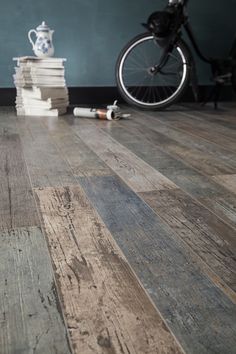 a pile of books sitting on top of a wooden floor next to a bike parked in front of a wall