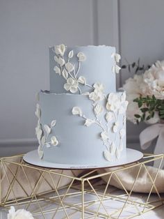 a three tiered cake with white flowers on the side and gold wire stand next to it