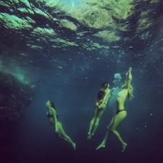 two women in bikinis swimming under water with their backs turned to the camera,