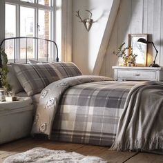 a bed with plaid comforter and pillows in a room next to a window,