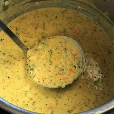 a ladle full of soup with broccoli and carrots in it is being stirred by a spoon