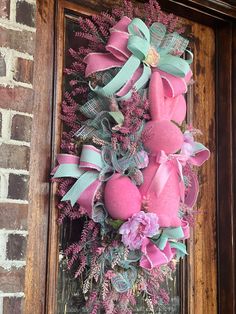 a wreath with pink and green decorations hanging on a brick wall next to a wooden door