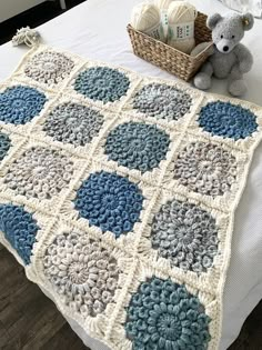 a crocheted blanket on top of a bed with a teddy bear next to it