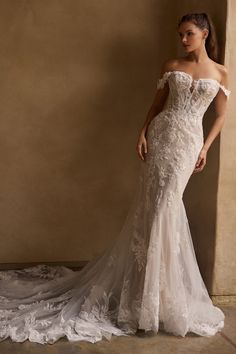 a woman in a white wedding dress standing next to a wall with her hands on her hips