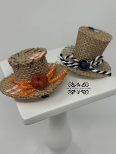 two straw hats are sitting on top of a white stand with an orange and black ribbon