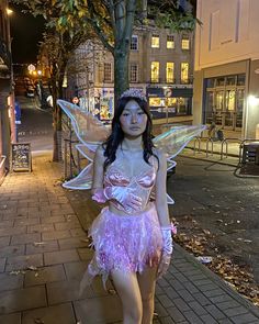 a woman dressed as a fairy standing on the sidewalk