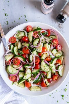 a white bowl filled with cucumber, tomatoes and onions on top of a table