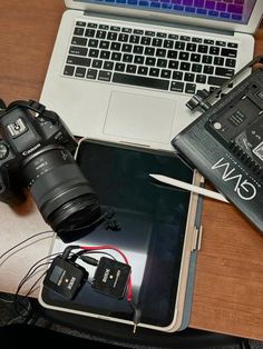 an open laptop computer sitting on top of a wooden desk next to a camera and other electronics