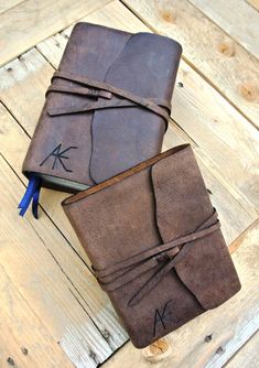 two brown leather journals sitting on top of a wooden table next to each other