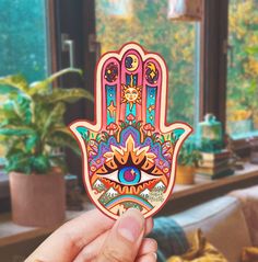 a person holding up a sticker with an image of a hamsa on it