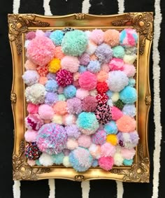 a gold frame filled with pom - poms on top of a black and white striped wall