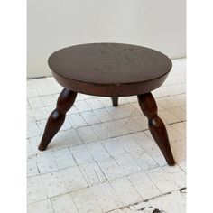 an old wooden stool with two legs on a white tile floor in front of a wall