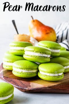 green macaroons are stacked on a wooden platter with an apple in the background