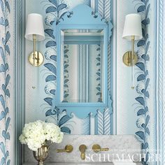 a bathroom with blue and white wallpaper, gold faucet, marble sink and mirror