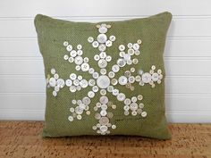 a green pillow with buttons on it sitting on top of a wooden table next to a white wall