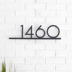 a metal number sign on a white brick wall next to a potted green plant