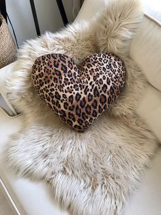 a leopard print heart pillow sitting on top of a white fur covered chair next to a lamp