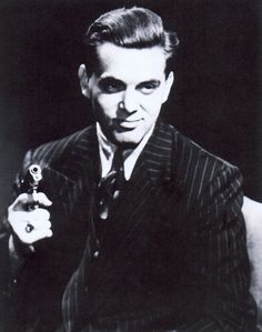 an old photo of a man holding a small object in one hand and looking at the camera