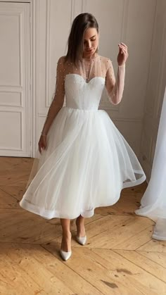 a woman in a white dress is standing on the floor with her hand up to her face