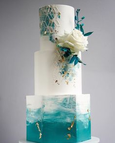 a three tiered white and blue cake with flowers on top